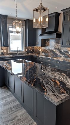 a large kitchen with marble counter tops and black cabinetry, along with two pendant lights hanging from the ceiling