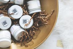 several small white jars sitting on top of a gold bowl filled with wood shavings