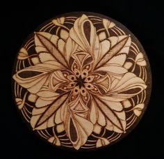 an intricately designed wooden plate on a black background with white and brown flowers in the center