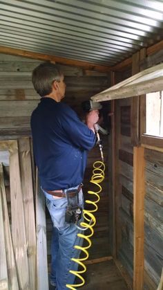 a man in blue shirt holding a hose inside of a wooden structure with wood walls