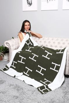 a woman sitting on a couch under a blanket that has the letters h in black and white