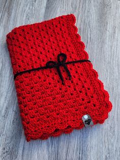 a red crocheted book with a black ribbon on it sitting on top of a wooden table