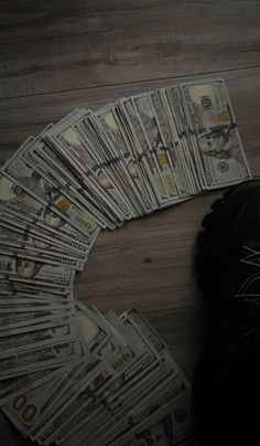 a pile of money sitting on top of a wooden floor next to a pair of black shoes