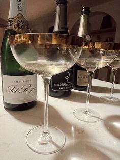 three wine glasses sitting on top of a table next to bottles of wine and a bottle of champagne