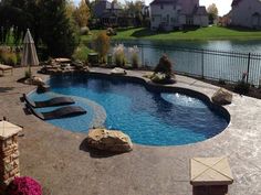 a backyard with a swimming pool surrounded by rocks and water features an outdoor lounge area