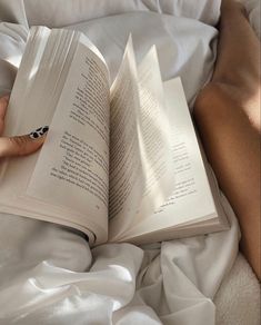 a person laying in bed reading a book with their hand on top of the book