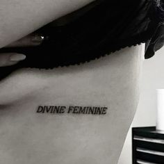 a woman's stomach with the word divine feminine tattooed on her lower side ribcage