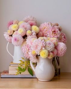 a white pitcher filled with pink and yellow flowers on top of a wooden table next to books