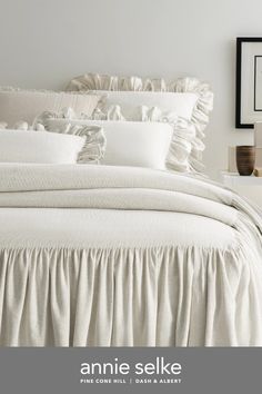 a white bed with ruffled sheets and pillows