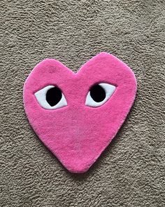 a pink heart with googly eyes is on the carpet and looks like it's made out of felt