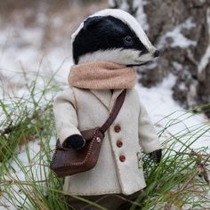 a small stuffed animal is dressed in a coat and scarf, sitting on the snow