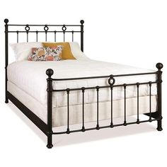 a black metal bed frame with white sheets and pillows on top of it, against a light wood floor