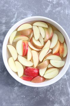 a white bowl filled with sliced apples on top of a gray countertop next to a knife