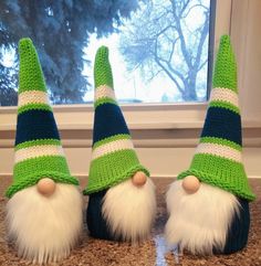 three green and white knitted gnomes sitting on top of a counter next to a window