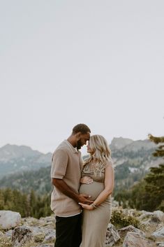 a pregnant couple standing on top of a mountain