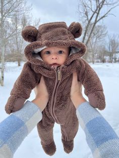 a baby in a bear costume being held up by someone's hands and wearing mittens