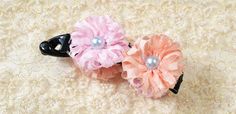 two pink and black hair clips with pearls on them sitting on a white lace surface