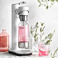 a pink beverage maker sitting on top of a table next to some glasses and plants