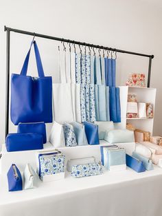 a table topped with lots of blue and white bags next to a shelf filled with purses