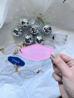 a person holding up a name tag next to some christmas balls and other items on a table