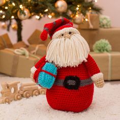 a crocheted santa clause sitting in front of a christmas tree with presents on the floor