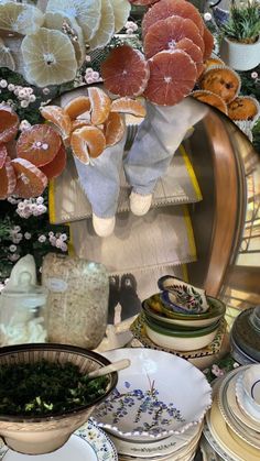 an assortment of plates and bowls with oranges on them in front of a floral display