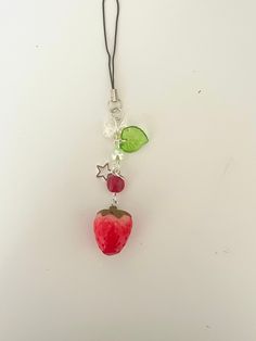 a red apple hanging from a black cord on a white surface with other items attached to it