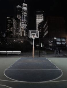 an empty basketball court at night with city lights in the background