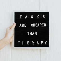 a hand is holding up a sign that says tacos are cheaper than therapy