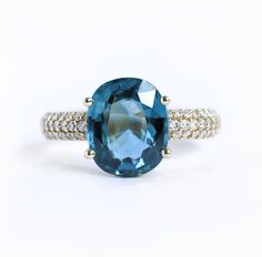 an oval cut blue topaz ring with two rows of diamonds around the band, set in 18k yellow gold