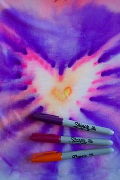 three pens sitting on top of a tie - dye shirt with the word sharpie written in it