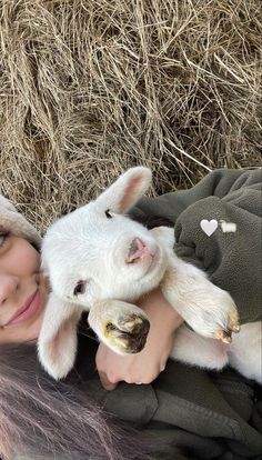 a woman is holding a baby goat in her arms while laying on hay bales