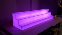 a purple couch sitting on top of a wooden table in front of a wall with lights