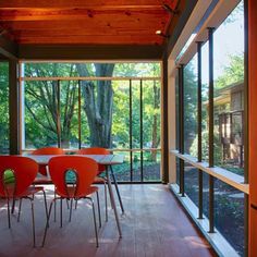 an orange table and chairs in a room with wood flooring, large windows, and wooden ceiling