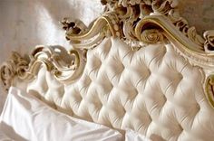 a white bed with gold trimmings and an ornate headboard on top of it