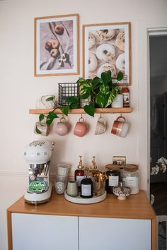 there is a coffee maker on the counter next to some cups and mugs with pictures above them