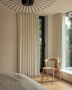 a chair sitting in front of a window next to a white curtained wall and wooden floor