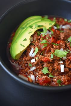 a black bowl filled with chili and an avocado