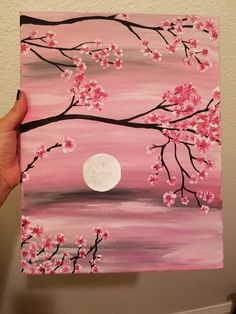 a person is holding up a painting with pink flowers and a full moon in the background