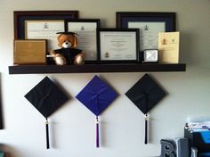 a shelf with some graduation caps and diplomas hanging on it's wall above a desk