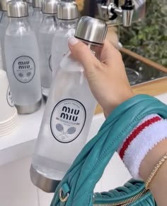 a person holding a water bottle in front of several bottles on a counter top,