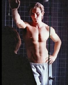 a shirtless man standing in front of a shower holding his hand up to the side