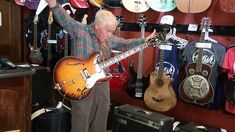 an older man is playing the guitar in his music store with other guitars and amps behind him