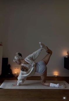 a woman is doing yoga on a mat in the middle of a room with candles