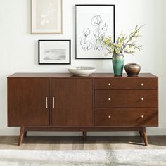 a wooden sideboard with two vases on top and pictures hanging above the drawers