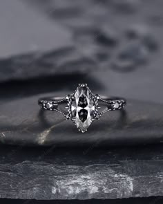 a white gold ring with an oval cut diamond surrounded by three smaller round diamonds, on top of a rock