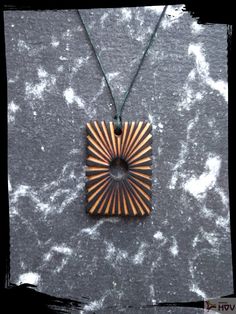 a necklace with a wooden design hanging from it's side on a gray surface