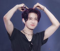 a young man with purple hair is holding his hands up to his head while wearing a black shirt