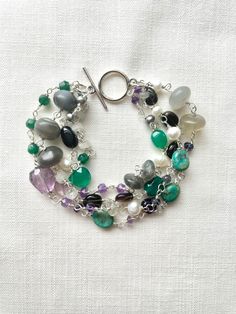 This multi-gemstone silver-plated wire-wrapped bracelet features gray moonstone, amethyst, labradorite, Smokey quartz, rainbow moonstone, green aventurine, green onyx, turquoise, iolite and freshwater pearls in a variety of shapes and sizes, set on 4 strands. This bracelet is 8 and 1/4 inches long and is finished with a 14 mm silver-plated toggle clasp.  This bracelet length can be altered to your specifications. These are genuine stones and may contain inclusions, and variations in size, color, Silver Fusion Beaded Bracelets With Natural Stones, Silver Amethyst Bracelets Hand Wrapped, Silver Natural Stone Round Beads Gemstones, Silver Natural Stones Round Beads Gemstones, Bohemian Sterling Silver Crystal Bracelet With Natural Stones, Bohemian Silver Amethyst Crystal Bracelet, Silver Amethyst Beaded Bracelets With Natural Stones, Silver Natural Stone Bracelet, Bohemian Silver Wire Wrapped Crystal Bracelet