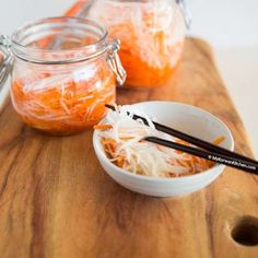 two bowls filled with shredded carrots on top of a wooden table next to chopsticks